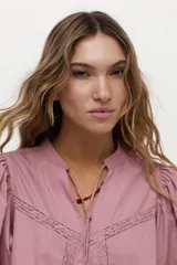 Blusa de algodón liviano color blanco, con detalles de puntilla en el frente, cuello mao con escote en V, cordón colgante y mangas largas abullonadas con puños ajustados.