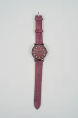 Reloj analógico con correa de cuero sintético color rosado pálido y caja a juego. La esfera es beige claro con números romanos en negro.