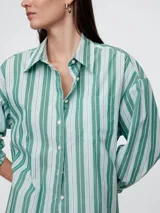 Camisa de corte oversize confeccionada en popelina, con diseño de rayas verticales en tonos verde y blanco. Presenta cuello clásico, cierre frontal con botones y bolsillo en el pecho.