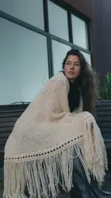 Ruana artesanal tejida en lana merino color crudo, con diseño de punto abierto en los bordes y flecos largos en todo el contorno.