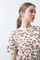 Remera de manga corta con estampado animal print en tonos marrones y beige sobre fondo blanco, con cuello redondo.