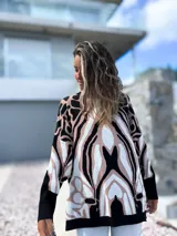 Sweater de punto con diseño oversize y estampado abstracto en tonos negro, beige y blanco. Presenta cuello redondo, mangas largas con puños ajustados y un corte holgado que cae suavemente sobre la figura.