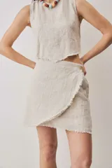 Falda cruzada tipo wrap color beige, de lino, con diseño asimétrico y bordes deshilachados. Cuenta con cierre de botón en la cintura.