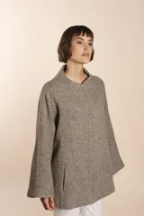 Capa de lana fina sin teñir, con estampado de espiga en tonos marrones y beige. Presenta cuello alto, mangas amplias, bolsillos laterales y pinzas en la parte delantera.
