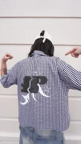 Camisa de corte boxy fit confeccionada en algodón con estampado de cuadros vichy en blanco y negro. Presenta un diseño gráfico artístico en color negro y blanco en la parte posterior.