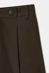Short de tiro alto color marrón, con pliegues frontales y detalle de botones decorativos en la cintura. Cuenta con bolsillos laterales y cierre frontal con cremallera y gancho metálico.