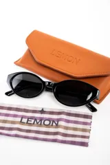 Lentes de sol Lemon de armazón ovalado color negro y cristales oscuros, con detalle de la marca en letras doradas en la patilla.