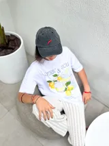 Remera oversize blanca de algodón con cuello redondo y hombros caídos. Estampado frontal con ilustración de dos vasos de limonada, limones y texto "CITRIC & SOUR".