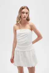 Vestido corto strapless de color blanco, con diseño drapeado en el torso y falda estilo globo con ruedo voluminoso.