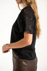 Remera de algodón peinado color negro, con mangas cortas de broderie con diseño calado y terminación festoneada. Presenta un corte oversize y cuello redondo.