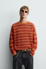 Jersey relaxed fit de punto calado con rayas horizontales en tonos naranja y amarillo. Tiene cuello redondo y manga larga con acabados irregulares.