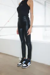 Pantalón de tiro alto confeccionado en bengalina engomada con acabado brillante. Presenta un corte ajustado, acceso lateral con cierre invisible y diseño de botamanga irregular.