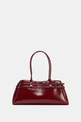 Bolso de hombro tipo city en color bordó con acabado brillante. Presenta un diseño estructurado con detalle de tiras decorativas con hebillas metálicas en los laterales y doble asa de hombro.
