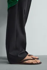 Sandalia tipo ojota o chancleta de goma, con base de color verde oscuro y tiras negras. Presenta una suela plana.