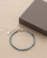 Pulsera elástica compuesta por una alternancia de cuentas de piedra natural en color turquesa y cuentas metálicas de acero en forma cúbica.