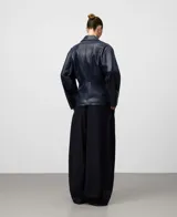 Chaqueta estilo biker de efecto cuero color azul marino, con solapa ancha, cierre cruzado frontal y cintura entallada. Presenta mangas largas y bolsillos delanteros con cremallera invisible.