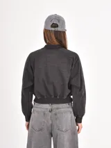 Campera tipo bomber de corte cropped, con cierre frontal, cuello redondo y puños elásticos, confeccionada en tela con efecto lavado.