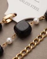 Pulsera de acero con baño de oro, adornada con cuentas cuadradas negras y pequeñas perlas blancas dispuestas alternadamente sobre una cadena eslabonada.