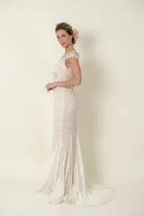 Vestido largo de novia color marfil, de encaje y tul, con apliques bordados y piedras. Tiene escote profundo y falda con cola.