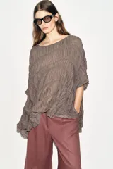 Top de cuello redondo color celeste con textura fruncida, mangas tipo capa y bajo asimétrico.