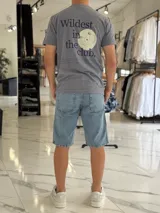 Remera gris melange de manga corta y corte clásico, con estampa en la espalda que dice "Wildest in the club" junto a un gráfico de un disco compacto.