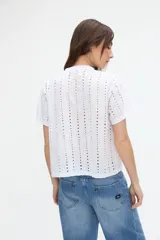 Blusa corta de broderie blanca, de manga corta, con cuello redondo y cierre frontal de botones.