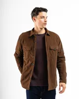 Sobre camisa de pana color marrón, con cierre frontal de botones, cuello clásico y dos bolsillos frontales con solapa y botón.