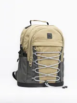 Mochila color arena con detalles en gris y negro. Cuenta con un compartimento principal con cierre, un bolsillo frontal con cordón elástico y bolsillos laterales de malla.