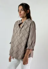 Blusa color beige con cuello mao, mangas 3/4 con puños elásticos y detalle de diseño geométrico texturizado en el frente.