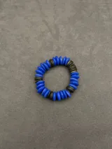 Pulsera elástica compuesta por cuentas de piedra natural en tonos azul vibrante y negro, intercaladas con pequeños discos metálicos dorados.