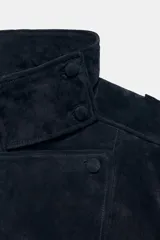Cazadora de piel gamuzada de color negro, con cuello subido, manga larga con trabillas en los hombros, bolsillos delanteros, bajo elástico y cierre frontal cruzado.
