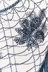 Capa o chal triangular de abalorios azul oscuro, con diseño de telaraña y tres motivos florales o de hojas bordados. El borde inferior tiene flecos largos hechos de abalorios.