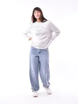 Remera de manga larga color crema con cuello redondo y un estampado central de un ramo de flores rosadas y naranjas en un jarrón azul oscuro.