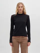 Polera de cuello alto confeccionada en tela rib color blanco, con mangas largas y hombreras. Presenta pespuntes en contraste en las terminaciones del cuello, hombros y puños.