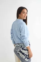 Buzo de tejido de punto con cuello redondo, diseño cropped y mangas largas con puños acanalados. Presenta una textura jaspeada en tono beige.