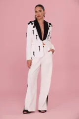 Pantalón de sastrería blanco de silueta fluida, con pliegues frontales y detalles laterales en negro.