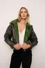 Chaqueta estilo bomber de cuero vacuno en color verde vintage, con cuello y forro interior de corderito al tono. Presenta cierre frontal completo y un diseño de inspiración retro con acabado texturizado.