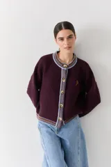 Cardigan de punto color bordó con cuello redondo, cierre frontal de botones y detalles de ribetes en contraste en cuello, puños y ruedo. Presenta un pequeño bordado de una raqueta de tenis en el pecho.