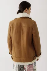 Campera tipo gamulán de cuero color camel con interior y solapas de corderito sintético en color crema. Presenta cierre frontal, bolsillos laterales y detalles de correas ajustables en los puños y la cintura.