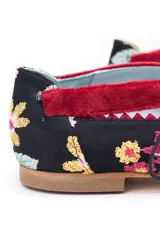 Zapatos tipo blucher de diseño artesanal, confeccionados en algodón con estampado floral multicolor sobre base negra. Presentan detalles en terciopelo color fresa, cierre con cordones rematados en borlas y suela de cuero.