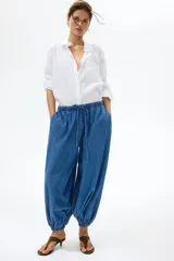 Pantalón tobillero de corte holgado en denim de algodón rígido, con cintura elástica con cordón de ajuste, bolsillos laterales discretos y piernas globo con elástico en los tobillos.