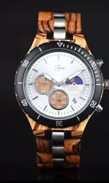 Reloj cronógrafo con caja de madera de zebrano y bisel técnico de acero negro. La esfera es plateada con subdiales de madera, indicador de fase lunar y fechador. La malla combina eslabones de acero inoxidable con madera de zebrano.