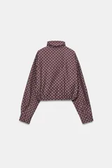 Cazadora negra con estampado de lunares blancos, cuello subido, manga larga, bolsillos delanteros, bajo ajustable con cordones y cierre frontal con cremallera y solapa con botones ocultos.
