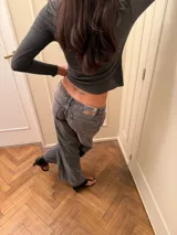 Pantalón de jean estilo wide leg, de tiro bajo, color gris lavado con efecto desgastado. Presenta corte recto y holgado en las piernas, con cierre frontal y bolsillos clásicos.