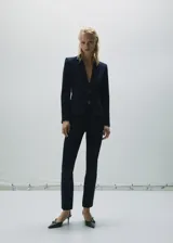 Blazer negro entallado de punto roma con solapas de muesca, hombros estructurados, abertura posterior y dos bolsillos de ribete delanteros.