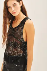 Top corto sin mangas con escote redondo, confeccionado en tul bordado con lentejuelas, piedras y canutillos. Presenta un diseño con flecos de mostacillas en el ruedo y una tira larga decorativa al cuello.