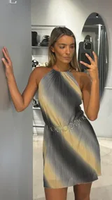 Vestido corto de escote halter con diseño plisado y estampado degradado en tonos gris y beige. Presenta un corte holgado y fluido, complementado con un cinturón de eslabones metálicos circulares.