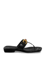 Sandalia plana negra tipo chinela con tira entre los dedos y tira ancha en el empeine adornada con herraje dorado y pieza de resina color ámbar.