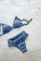 Conjunto de bikini de dos piezas con efecto brillante y estampado tipo tie-dye en tonos azules. El top es de estilo triángulo con breteles regulables y cierre de gancho en la espalda. La bombacha es de tiro alto y corte vedetina.