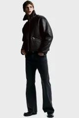 Campera de tejido revestido con acabado efecto cuero, cuello de solapa con forro de sherpa, cierre frontal con cremallera metálica y bolsillos laterales con cierre.